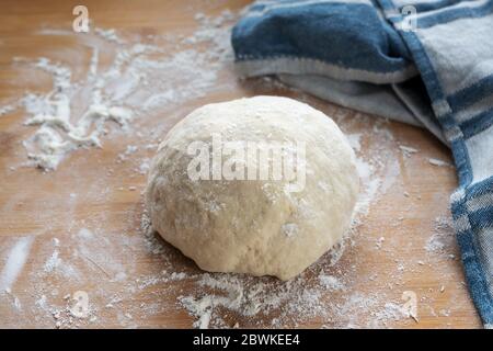 Roher Hefeteig für Brot oder Kuchen, bereit, auf einem hölzernen Backbrett etwas Mehl und ein blaues Küchentuch aufzugehen, ausgewählter Fokus, schmale Schärfentiefe Stockfoto