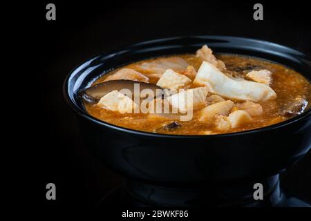 Japanische Suppe mit Huhn, Ei, Simeji-Pilzen und Aubergine auf dunklem Hintergrund in einem schwarzen Teller. Nahaufnahme Stockfoto