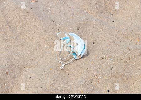 Eine ausgeworfene chirurgische Schutzmaske am Sandstrand. Schmutzige gebrauchte medizinische Maske am Strand nach dem Coronavirus covid-19 e verwendet werden verworfen Stockfoto