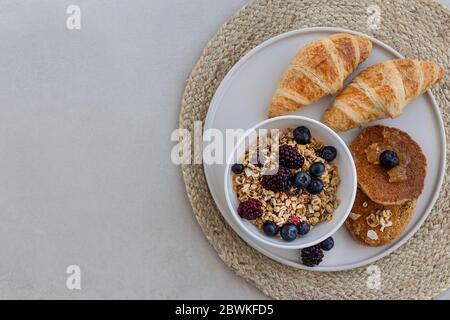 Topview Bild von gesunden und nahrhaften Frühstücksplatte mit Müsli, Haferflocken Pfannkuchen und Croissants. Horizontale Zusammensetzung. Negativer Raum. Stockfoto