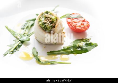 Fischrolle aus Scholle Filet gefüllt mit Stampfsellerie und Rucola, gegrillte Tomaten, Rucola Salat, Sesam und Dressing auf einem weißen Teller, festliche Appe Stockfoto