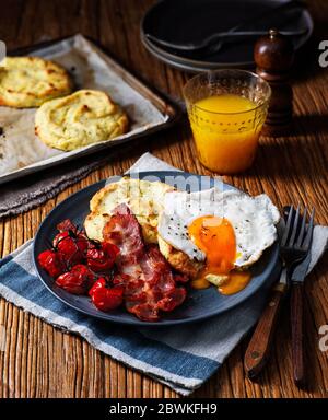 Warmes Frühstück mit Kartoffelkuchen, Tomaten auf der Rebe, Speck und ein Spiegelei mit Orangensaft Stockfoto