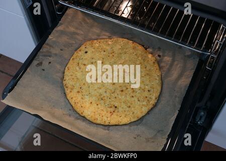 Gebackene Pizzabruste aus geschreddertem Blumenkohl und Käse auf einem Backblech im Ofen, gesunde Schlankheitsalternative für Low Carb und ketogene Ernährung, Sel Stockfoto