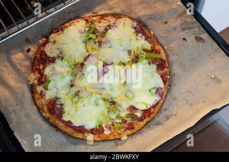 Gebackene Pizza aus Blumenkohlenkruste mit Salami und Käse frisch aus dem Ofen, ausgewählte Fokus, schmale Schärfentiefe Stockfoto