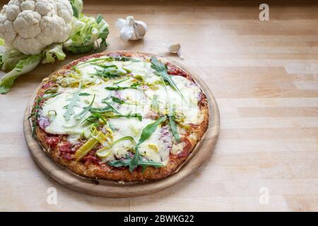 Pizza mit Kruste aus geschreddertem Blumenkohl auf Holzbrett, Alternative für kohlenhydratarme oder ketogene Ernährung, Kopierraum, ausgewählter Fokus, schmale Tiefe o Stockfoto