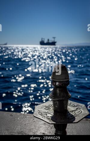 Die Spitze der schönen scripted Hookah auf dem Hintergrund des verschwommenen blauen Wasser des Roten Meeres in Jordanien und Silhouette des großen Schiffes weit weg. Erstaunlich ruhigen Winter sonnigen Tag, contre-jour Bild Stockfoto
