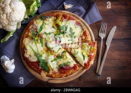 Low Carb Pizza mit einer Kruste aus zerkleinerten Blumenkohl auf einem dunklen rustikalen Holztisch, alternative Rezept ohne Kohlenhydrate für eine ketogene Ernährung, Hi Stockfoto