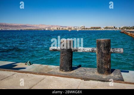 Golf von Aqaba vom Hafen aus gesehen, Jordanien. Einige Hotels in der vordersten Reihe und das kristallblaue Wasser des Roten Meeres, sonniger Winternachmittag, verschwommene Beton- und Metallausrüstungen Stockfoto