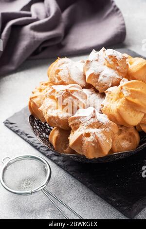 Profiterole mit Pudding und Puderzucker auf einem Teller. Beton grauer Tisch. Kopierbereich Stockfoto