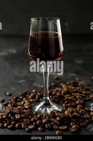 Starker dunkler Kaffeelikör mit gerösteten Kaffeebohnen. In einem hohen Stapel auf schwarzem Hintergrund Stockfoto
