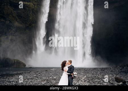 Hochzeitspaar in der Nähe des Skogafoss Wasserfalls. Hochzeit in Island. Der Bräutigam küsst die Braut. Stockfoto