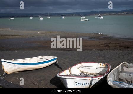 Dingys am Strand bei Boote in der Ferne, Kawhia, Nordinsel, Neuseeland. Boote in der Ferne in Kawhia Hafen festgemacht. Stockfoto