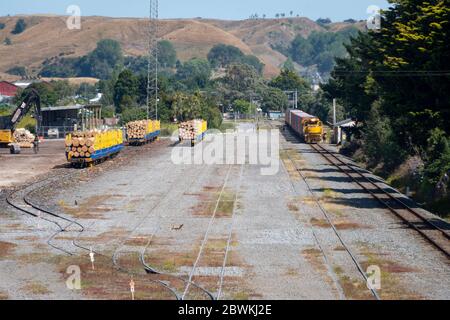 Zug vorbei an Güterbahnhof in Whanganui, North Island, Neuseeland. Auf den Wagen im Hof geladene Protokolle. Stockfoto