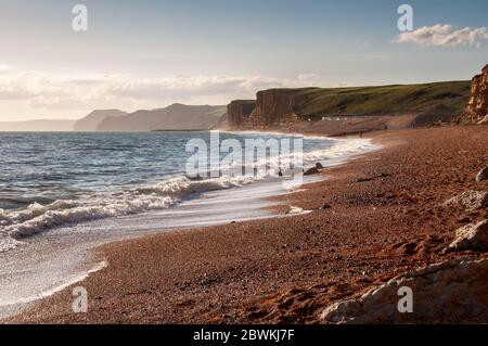 Die Leute laufen am Strand von Burton Freshwater entlang, unter den Sandstein-Ostklippen von West Bay in der Nähe von Bridport an Dorset's Jurassic Coast. Stockfoto