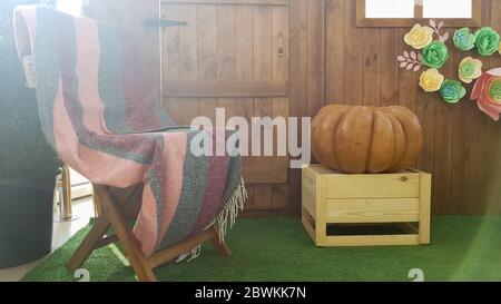 Schöne Herbstlandschaft mit einem Kürbis und einem hölzernen Vintage-Stuhl mit einem Plaid auf einer Terrasse in der Nähe eines Holzhauses Stockfoto