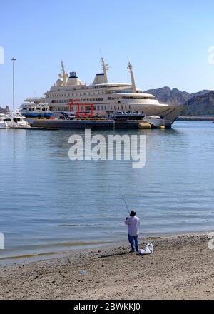 Einheimische Fischer am Strand mit der Al Said Royal Yacht im Hintergrund, Maskat, Oman Stockfoto