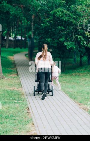 Konzept Familie, Kind und Elternschaft. Glückliche Mutter, die mit Kinderwagen im Park von hinten geht. Stockfoto