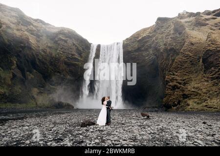 Hochzeitspaar in der Nähe des Skogafoss Wasserfalls. Hochzeit in Island. Der Bräutigam küsst die Braut. Stockfoto