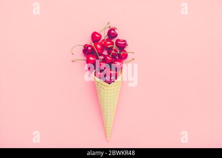 Frische Kirschen in Waffelzapfen Eiscreme-Kegel gefüllt mit frischer Süßkirsche auf rosa Hintergrund. Draufsicht. Kopierbereich. Sommer Creative Concept Flat Stockfoto
