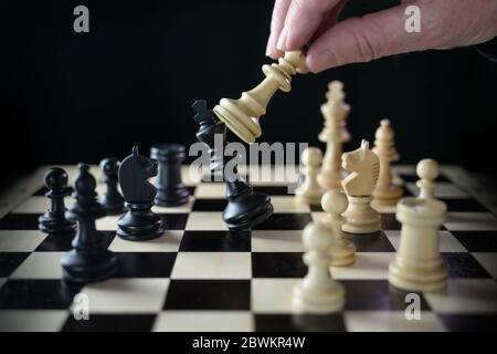 Menschliche Hand spielt Schach und besiegt den König, Schachmatt auf dem Schachbrett vor einem schwarzen Hintergrund, ausgewählten Fokus, enge Tiefe des Feldes Stockfoto