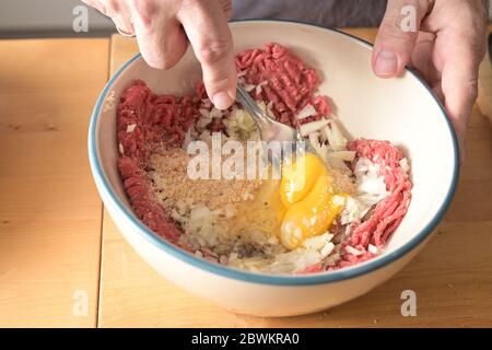 Hände eines Mannes mischen Hackfleisch und andere Zutaten mit einer Gabel in einer Schüssel, für die Herstellung von Fleischbällchen, ausgewählten Fokus, schmale Schärfentiefe Stockfoto