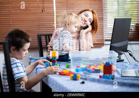 Eine junge weibliche Mutter versucht, während der Zeit der Selbstisolierung im Zusammenhang mit der Coronovirus-Pandemie an einem Computer an einer Remote-Arbeit zu arbeiten, so Stockfoto