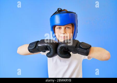 Ein Junge mit grünen Augen trägt einen Boxhelm und Handschuhe auf blauem Hintergrund. Stockfoto