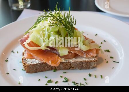 Vollkornbrot mit Lachs, Gurke, Meerrettichflocken und Dillgarnierung auf einem weißen Teller serviert, ausgewählte Fokus, schmale Schärfentiefe Stockfoto