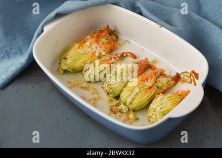 Gefüllte Zucchini oder Zucchini-Blumen mit Parmesan-Käse und Petersilie gebacken garnieren in einer Kasserolle mit einer blauen Serviette, Kopierraum, ausgewählte Focu Stockfoto