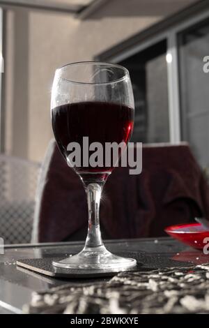 Ein Glas köstlicher Rotwein mit Sonneneinstrahlung auf dem Glas und schwarz-weiß-Feeling außer roter Farbe Stockfoto