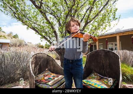 6 Jahre alter Junge spielt Geige außerhalb seines Hauses Stockfoto