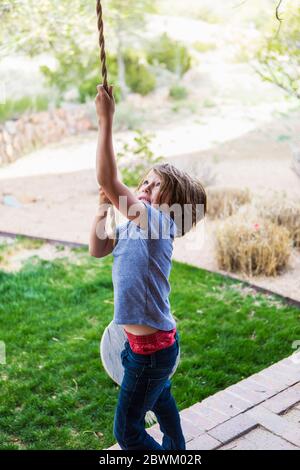 6 Jahre alter Junge mit einer Seilschaukel auf einer großen Veranda im Schatten. Stockfoto