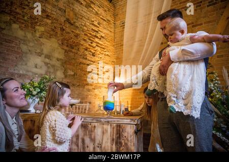 Familie Gießen farbigen Sand in Glas während der Namensgebung Zeremonie in einer historischen Scheune. Stockfoto