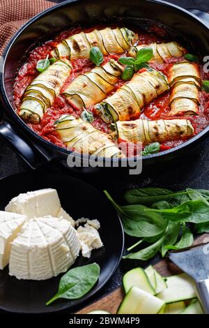 Gesundes italienisches Rezept von gerollten Zucchini-Streifen mit einer Füllung aus Ricotta mit Baby-Spinat gemischt, frische Basilikumbleck in Tomatensauce gebacken serviert auf Stockfoto
