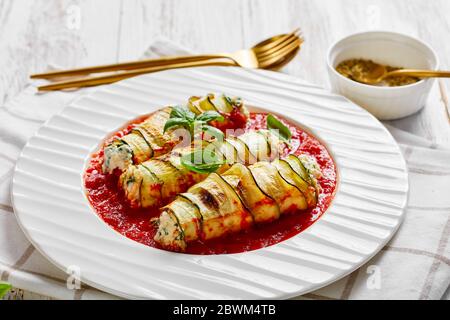 Low-Carb Zucchini Lasagne Brötchen mit Ricotta-Mischung aus frischem Baby-Spinat gefüllt, Basilikum in Tomatensauce gebacken serviert auf einem weißen Teller mit Besteck auf einem Stockfoto