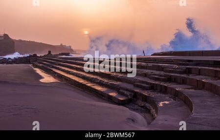 Sonnenuntergang und stürzende Wellen über den Stufen des natürlichen Schwimmbades an der Küste von Bajamar Teneriffa Kanarische Inseln. Stockfoto