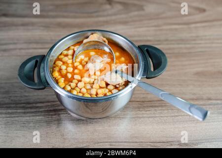 Traditionelle türkische Küche Kichererbsen in Topf mit Schöpfkelle auf braunem Tisch. Kichererbsensuppe. Stockfoto