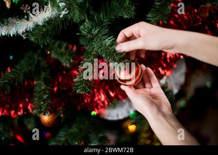 Mädchen hängt eine schöne rote Kugel auf einem Weihnachtsbaum. Nahaufnahme Stockfoto