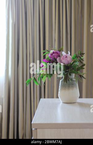 Pinke Pfingstrosen in einer Vase und graue Vorhänge im Hintergrund Stockfoto