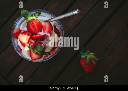 Sommerdessert im Glas mit Mascarpone-Creme und Erdbeeren auf einem dunklen Gartentisch, von oben geschossen Stockfoto