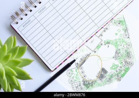 Wochenplaner mit Stift, Hauspflanze im weichen Fokus und Computer-Garten-Design Zeichnung Skizze. Landschaftsbau architektonische Projektabwicklung, Gartengestaltung Landschaftskonzept Stockfoto