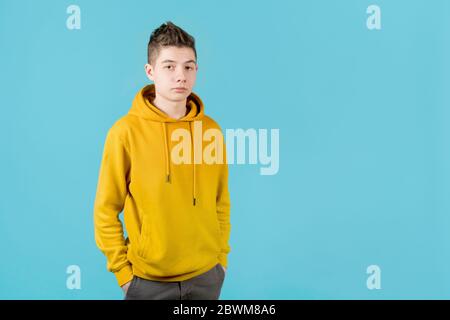 Ernst junger Kerl in einem gelben Sweatshirt auf einem blauen Hintergrund Stockfoto
