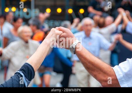 Barcelona, Spanien. Ansicht von älteren Menschen, die Hände halten und den Volkstanz Sardana auf der Plaza Nova, Barcelona, Spanien tanzen. Alte Hände vor dem Blurre Stockfoto