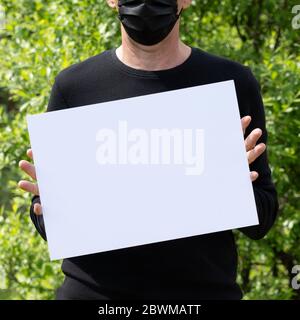 Mann in medizinischen schwarzen Maske hält ein weißes Banner mit Platz für Text isoliert auf schwarz . Stockfoto