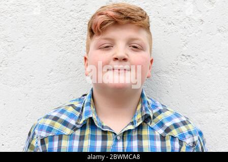 Rothaariger Junge. Ein Junge in einem karierten Hemd steht auf einem Wandhintergrund. Stockfoto
