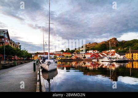 Halden, Norwegen. Blick auf die beleuchteten Häuser und Yachten mit der Festung Fredriksted im Hintergrund in Halden, Norwegen am Abend bei bewölktem Sonnenschein Stockfoto