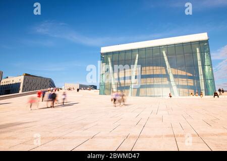 OSLO, NORWEGEN - 23. JUNI 2019: Blick auf das Opernhaus in Oslo, Norwegen während des sonnigen Tages. Bewegung verschwommen Menschen vor der Glasfassade der Opera Ho Stockfoto