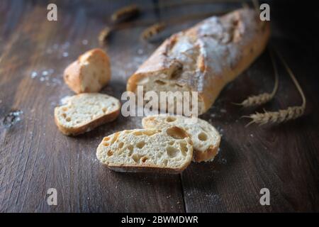 Frisches Baguette oder französisches Brot mit Zwiebeln gebacken, halb geschnitten, auf dunklem rustikalem Holz, ausgewählter Fokus, schmale Schärfentiefe Stockfoto