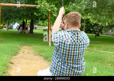 Junge mit chirurgischer Maske auf der Schaukel im Bereich von ​​the divetto durch ein rot-weiß gestreiftes Absperrband um den Spielplatz. Einzäunung rot und weiß Stockfoto