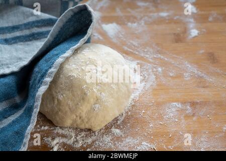 Hefeteig für Brot oder Kuchen wird mit einem Küchentuch abgedeckt, um sich auszuruhen und auf einem hölzernen Backbrett, Kopierraum, ausgewählten Fokus, schmale Tiefe steigen Stockfoto